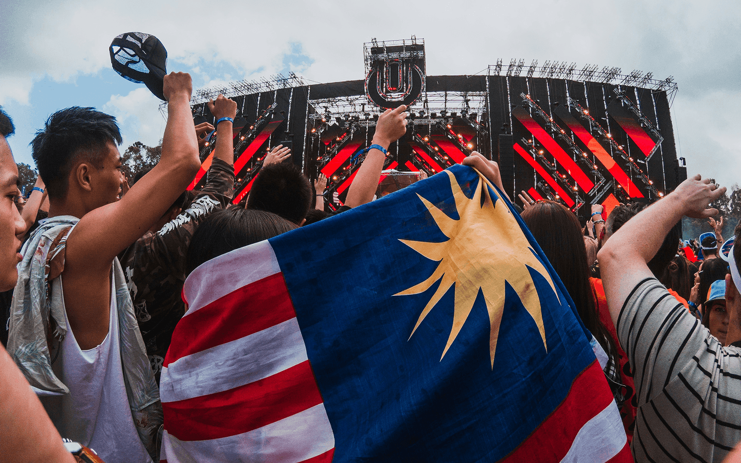 Crowd at an outdoor festival stage holding up a flag