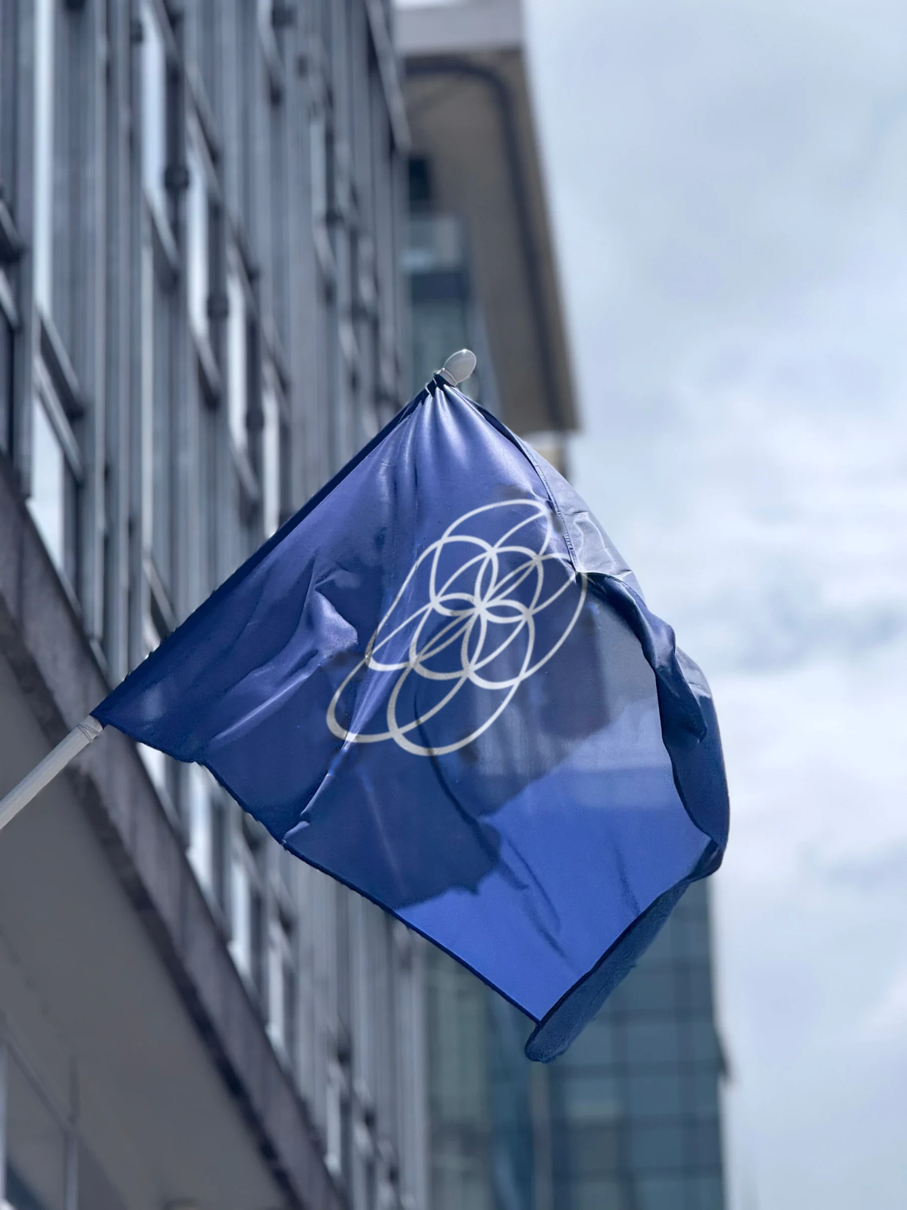 Earth Flag with interlocking white rings on blue on a building facade pole (digital composite)